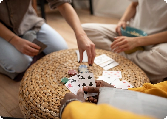 Mensen zitten rond een gevlochten tafel te kaarten. De ene persoon houdt de speelkaarten vast, terwijl de andere naar de pokerfiches reikt. De sfeer is ontspannen en gezellig.